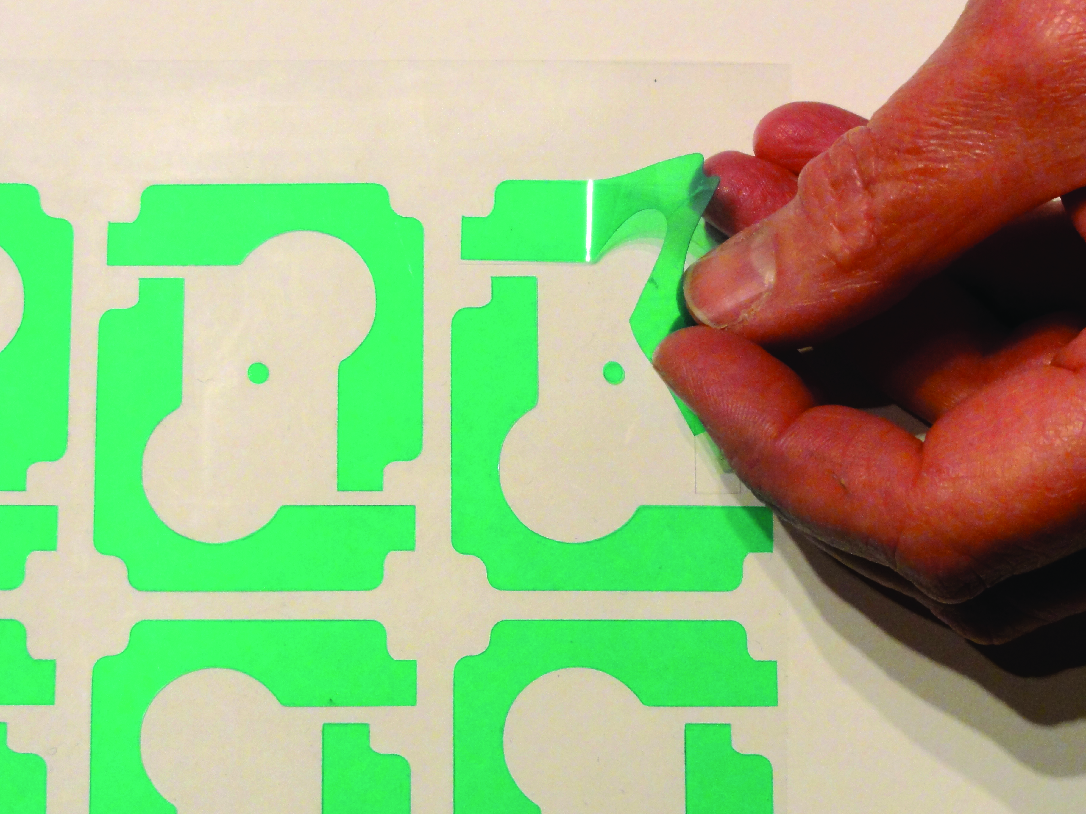 Hand peeling a green pre-cut masking shape from a backing sheet